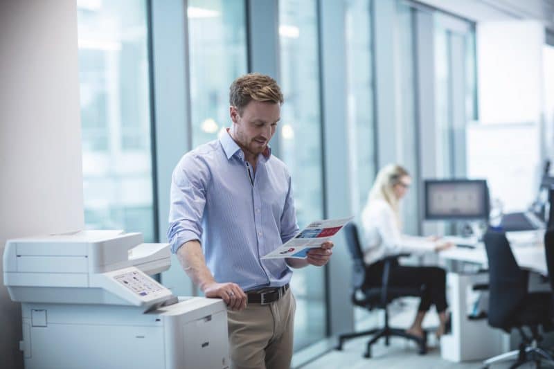 Medewerker staat naast een Brother printer en bekijkt een pas afgedrukt document